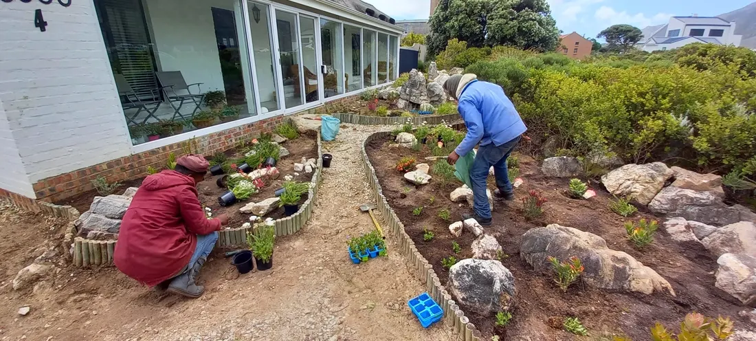 Crew planting a rock-edged bed beside a house